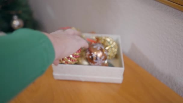La mano femminile raccoglie il baule di Natale scintillante da una scatola e lo appende a un albero di Natale. - Slow Motion — Video Stock