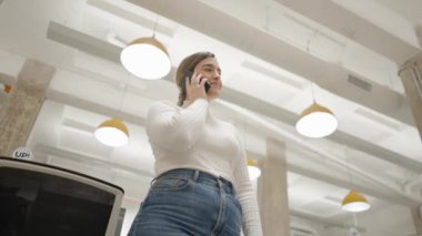 Beyaz kazaklı beyaz iş kadını modern ofiste telefonla konuşuyor. Düşük açılı görüş.