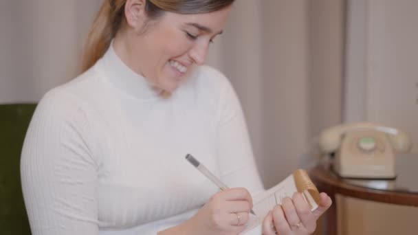 Lachende Europese zakenvrouw of student die briefjes van dichtbij schrijft. Jonge vrouw neemt notities in papieren notitieboekje, het schrijven van creatieve idee en glimlachen geïnspireerd en gelukkig. — Stockvideo