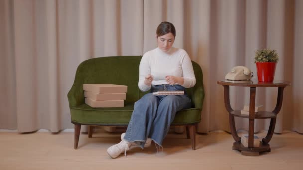Jovem empresária caucasiana tomando notas em seu caderno enquanto se senta em um sofá estilo retro — Vídeo de Stock