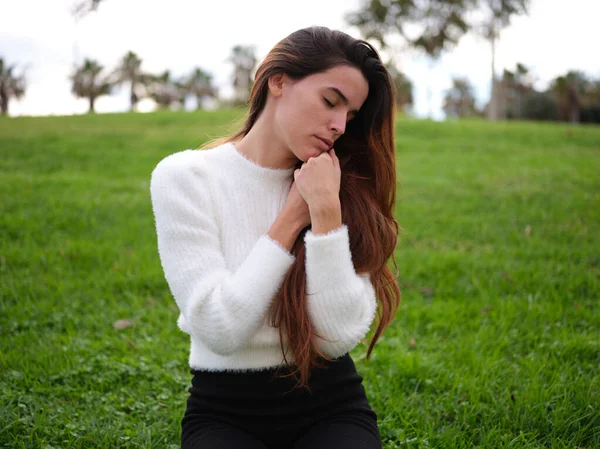 Uma jovem mulher relaxando no parque com as mãos dobradas no peito e os olhos fechados. — Fotografia de Stock