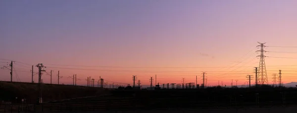 Panoramic sunset with the silhouettes of electric towers on the background — Stock Photo, Image