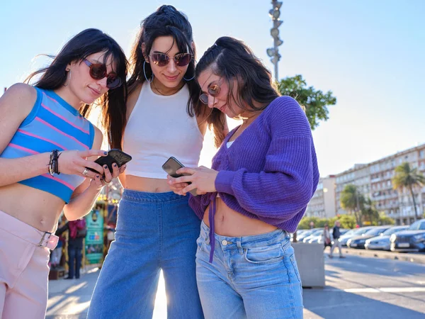 Tři mladé ženy na sobě vintage styl oblečení pomocí mobilních venku — Stock fotografie