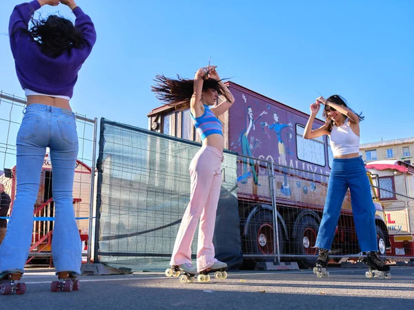 Three friends dancing wearing skates in the street next to a circus in a sunny day — Stock Photo, Image