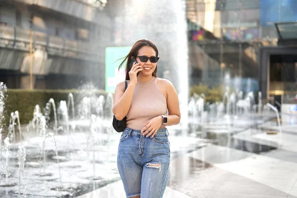 Mujer asiática en gafas de sol hablando con el móvil de pie al aire libre — Foto de Stock