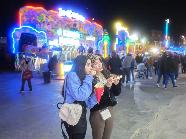 Menina apontando para a frente e falando com um amigo e comer em uma feira à noite — Fotografia de Stock