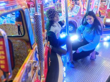 Bir gece fuarında şehvetli bir pozla oturan iki kadın.