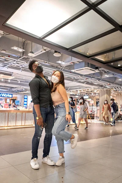 Vertikales Foto von Freunden mit Maske, die sich umarmen, während sie in einem Einkaufszentrum posieren — Stockfoto