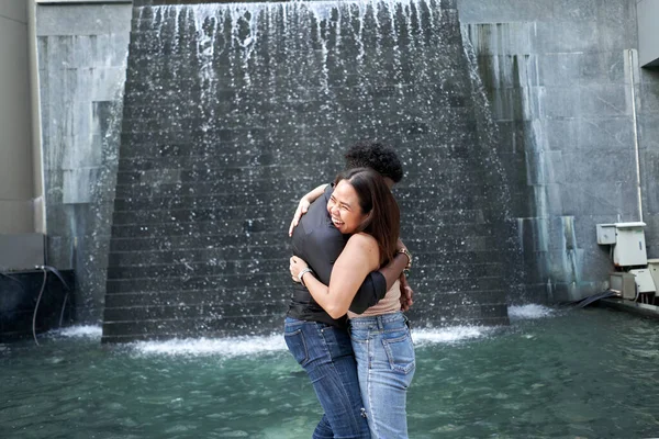 Amigos multiétnicos abrazándose junto a una cascada artificial en un centro comercial moderno —  Fotos de Stock