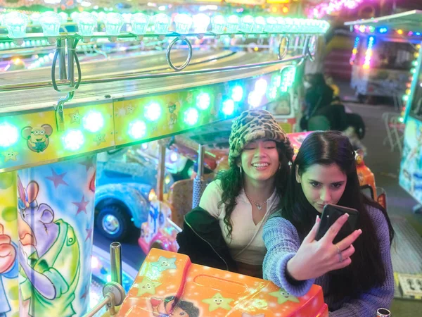Amigos sentados em uma atração de feiras enquanto tiram uma selfie à noite — Fotografia de Stock