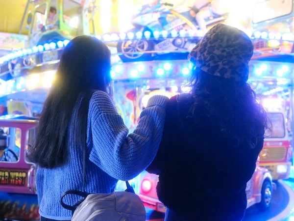 Duas mulheres abraçando enquanto olham para um carrossel em uma feira noturna — Fotografia de Stock