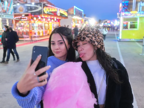 Vänner som tar selfie medan de grillar och håller i ett sockervadd på en nattmarknad — Stockfoto