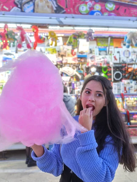 Mulher latina comendo um algodão doce enquanto está de pé em uma feira de noite — Fotografia de Stock