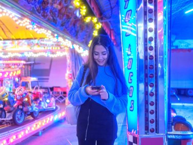 Geceleri çılgın bir arabanın yanında cep telefonu kullanan gülümseyen bir kadın.