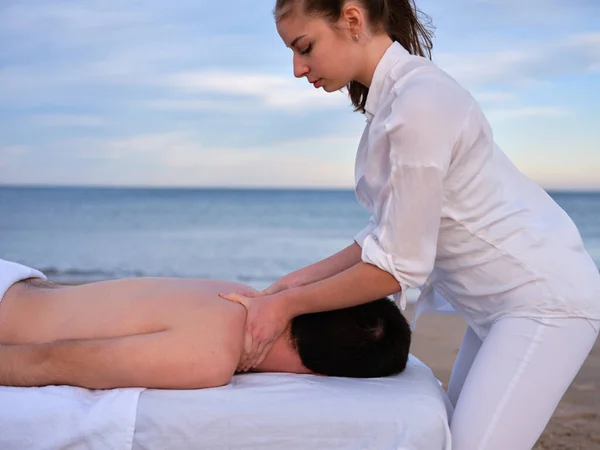 Junger Chiromassage-Therapeut gibt jungen Mann an einem Strand in Valencia eine Schultermassage. — Stockfoto