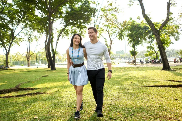 Casal multirracial andando em um parque segurando uns aos outros costas — Fotografia de Stock