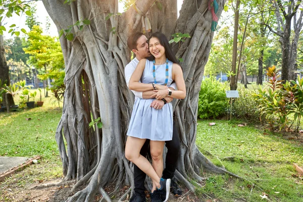 Man kissing her partener next to an ancient tree in a park during sunset — Foto Stock