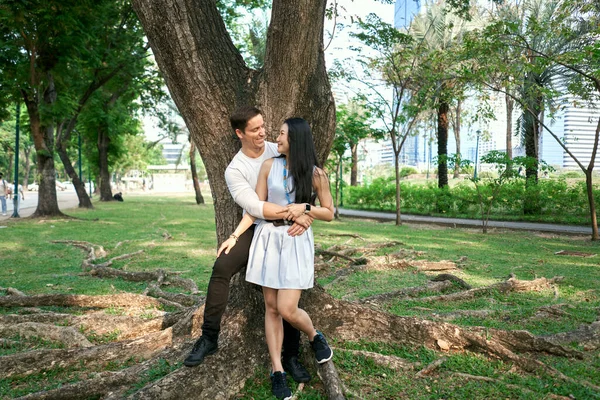 Multiethnic couple in love embracing while leaning against a tree together — Foto Stock