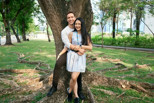 Newly married multiracial couple embracing against a tree — Foto Stock