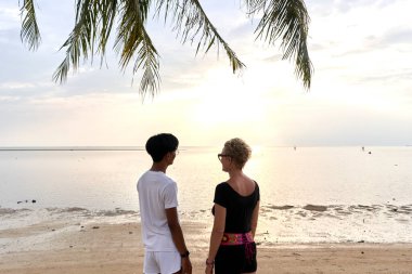 Tropik bir plajdan gün batımını seyreden iki aşığın arkası.