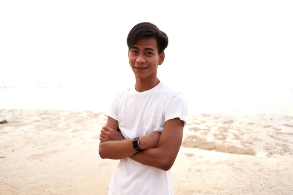 Asian young man with the arms crossed wearing a digital bacelet on a beach — стокове фото
