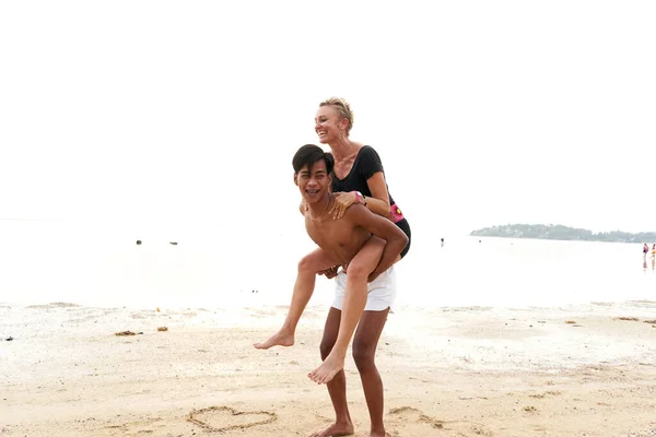Asian man piggyback riding to a his couple in a sandy tropical beach —  Fotos de Stock