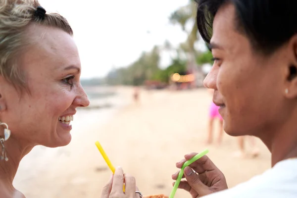 Lovers looking to each other while sharing a coconut juice in the beach — ストック写真