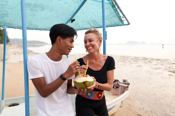 Smiling multicultural couple sharing the juice of a coconut — Fotografia de Stock