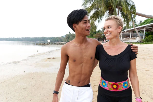 Smiling multicultural couple walking along a tropical beach — Fotografia de Stock