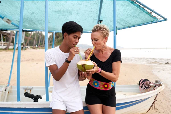 Multicultural couple drinking the juice of a natural coconut with a straw. — Fotografia de Stock