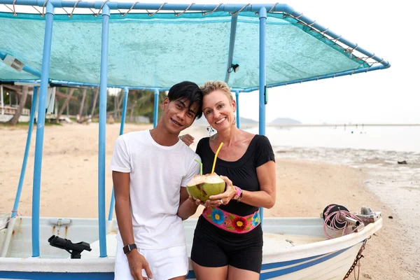 Multicultureel koppel kijkend naar camera terwijl ze kokosnoot drinken op het strand — Stockfoto