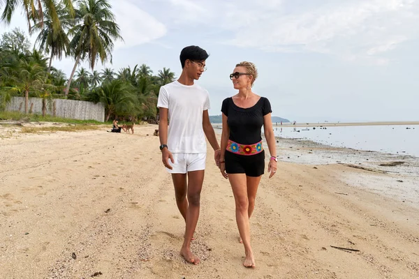Multicultureel koppel wandelen langs een paradijs strand hand in hand — Stockfoto