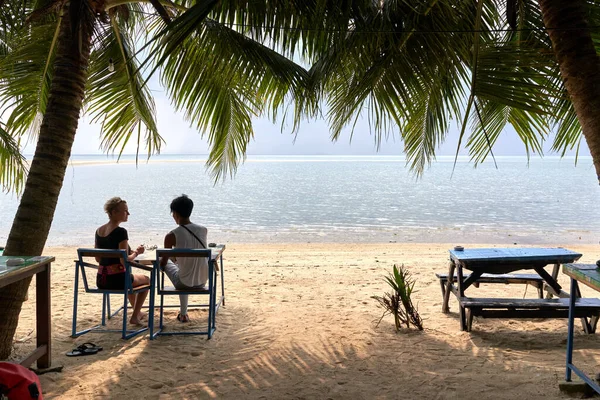 Wielokulturowa para siedząca na plaży patrząc na horyzont podczas rozmowy — Zdjęcie stockowe