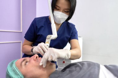 Doktor klinikteki bir hastaya güzellik tedavisi için lazer uyguluyor.