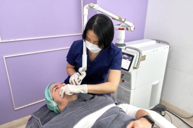 Lazer makineli bir oda ve müşteriye güzellik tedavisi uygulayan bir doktor.