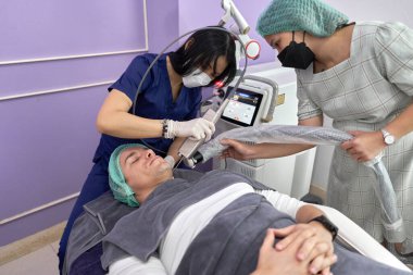 Doktor ve asistanı lazer kullanarak bir hastaya güzellik tedavisi uyguluyor.