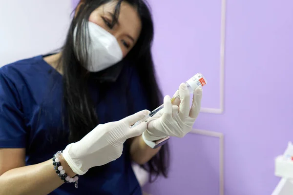 Lékař připravuje injekci pro pacienta na klinice během používání mobilního telefonu — Stock fotografie