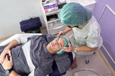 Hemşire bir müşteriye yüz güzelliği tedavisi için krem sürüyor.