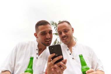 Eşcinsel çift dışarıda bira içerken cep telefonunu kullanıyor.