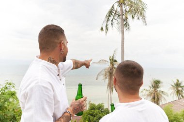 Eşcinsel adam ufku işaret ediyor. Denize bakan eşinin yanında.