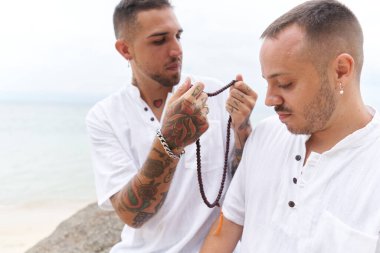 Sahilde kolye takmaya çalışan iki eşcinsel.