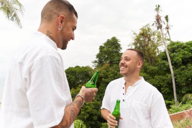 Gülümseyen eşcinsel çift dışarıda konuşurken bira içiyor.