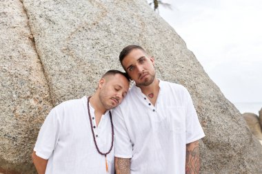 Eşcinsel bir adam kumsalda başıyla partnerinin omzuna yaslanıyor.