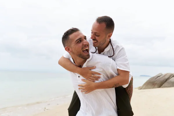 Close up retrato de um homem piggybacking seu gay parceiro no um praia — Fotografia de Stock