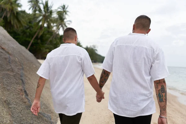 ゲイのカップルの後ろに手をつないでビーチに沿って歩く — ストック写真