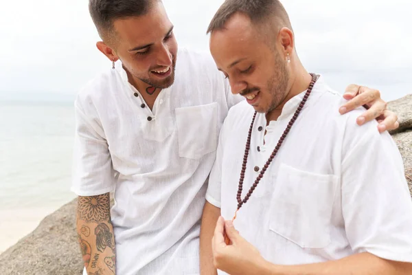 Gay uomo felicemente guardando un collana accanto a la sua partner su un tropicale spiaggia — Foto Stock