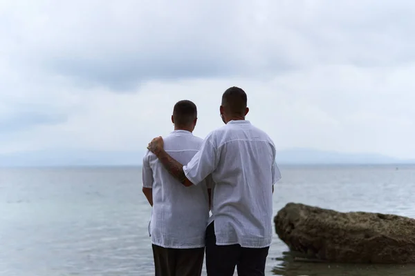 Gay couple gazing at the horizon of the ocean as they embrace in the evening — Stock Photo, Image