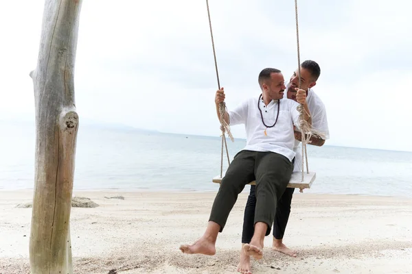 Gay uomo oscillando la sua partner in il mezzo di un tropicale spiaggia — Foto Stock