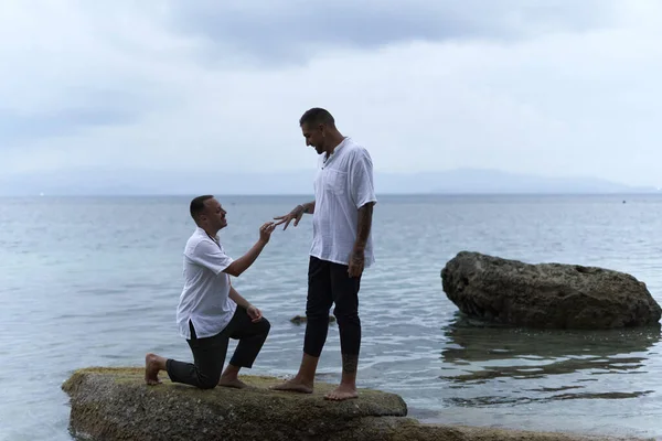 Gay uomo su la sua ginocchia chiedendo il suo partner per sposare lui accanto per il mare — Foto Stock