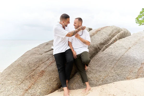 Homoseksüel bir adam tropik bir plajda ortağına top kolyesi veriyor.